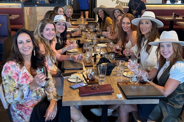 Group of women sitting at a restaurant table, holding wine glasses and smiling.