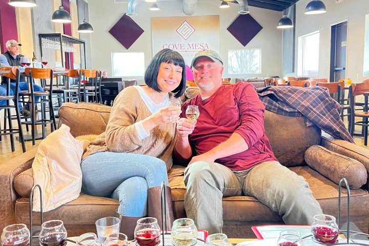 A couple on a sofa holding wine glasses in a cozy tasting room with tables in the background.