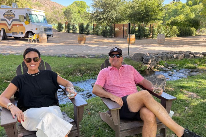 Two people sitting on wooden chairs outdoors with a food truck in the background.