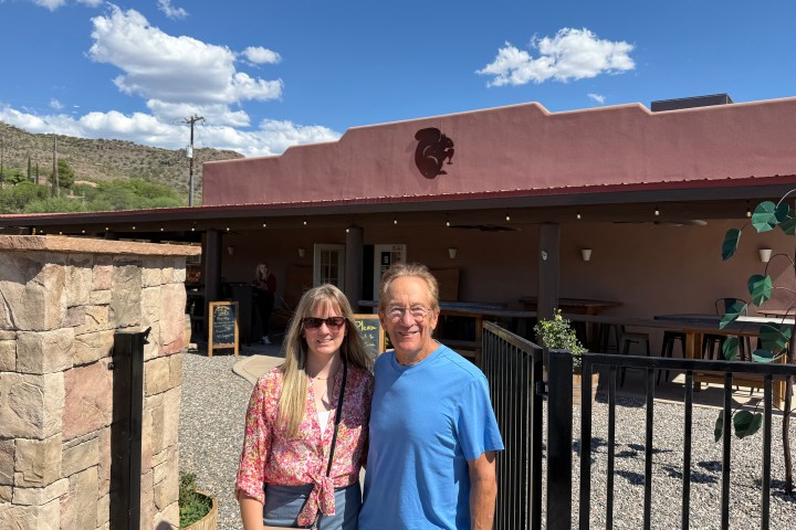 Two people standing in front of a building with a desert landscape in the background.