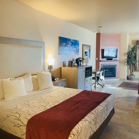 Hotel room with a large bed, red throw, desk, TV, and fireplace.