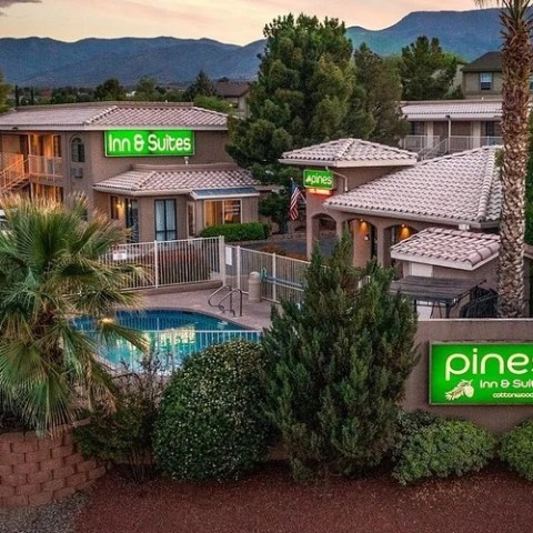 Hotel with palm trees, pool, and signage reading 'Pines Inn & Suites' amid a mountain backdrop.