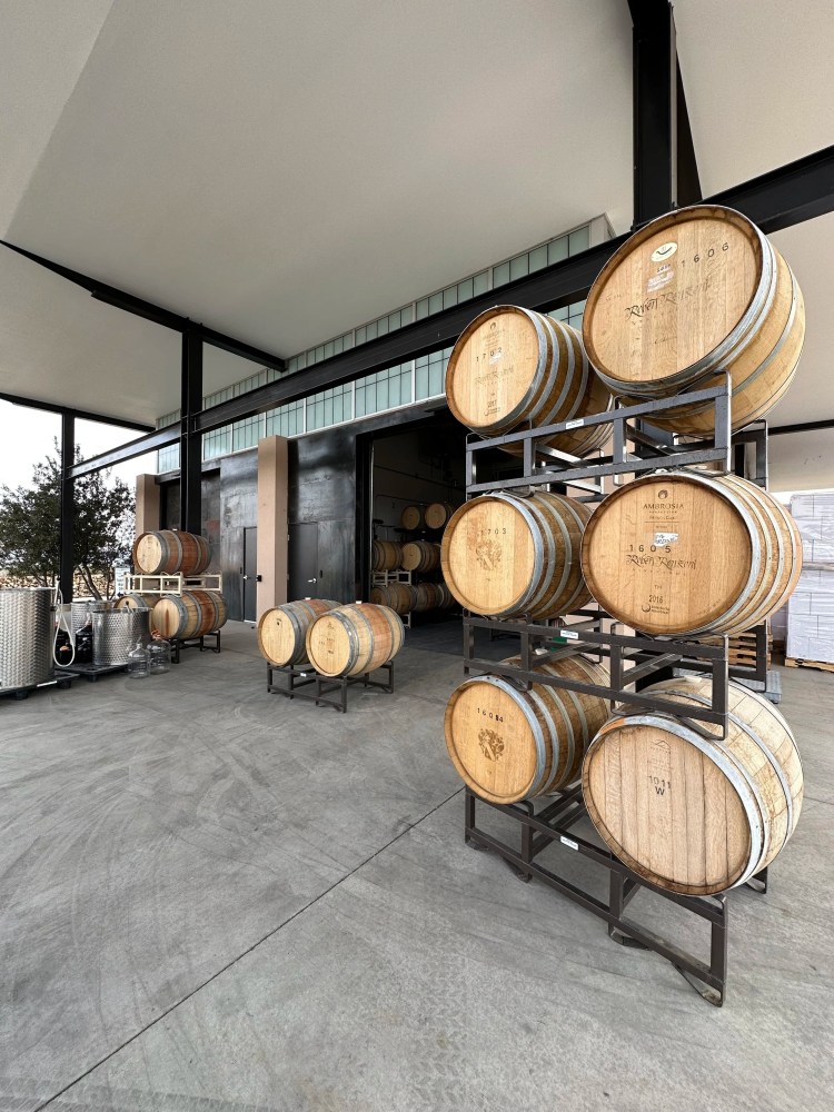Stacked wooden barrels in a warehouse with high ceiling and metal beams.
