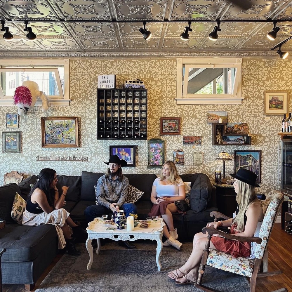 Four people sitting in a cozy, art-filled living room with patterned wallpaper and tin ceiling.