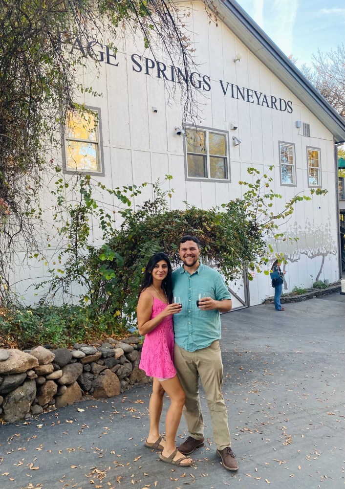 Couple holding wine glasses in front of a building labeled 'Sage Springs Vineyards'.