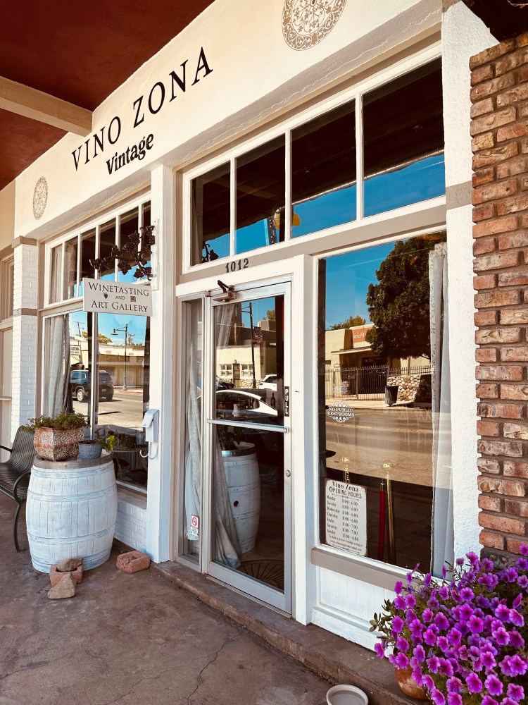 Entrance to Vino Zona with wine barrels and purple flowers outside.