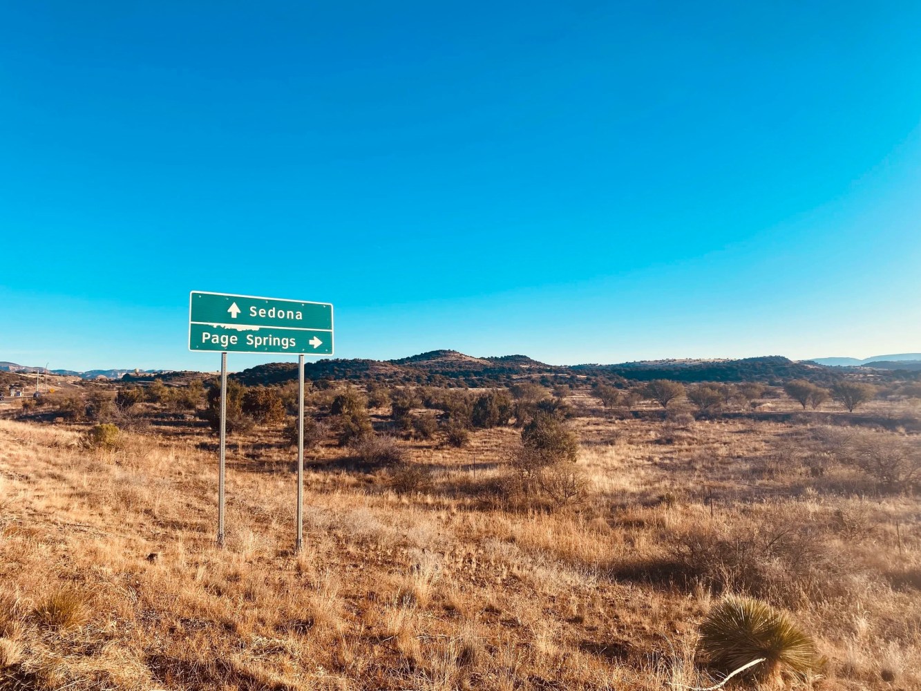 Road sign for Sedona and Page Springs in a desert landscape under a clear blue sky.
