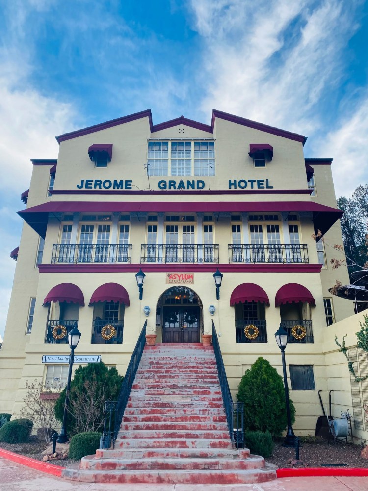 Facade of Jerome Grand Hotel with red awnings and central staircase under a blue sky.