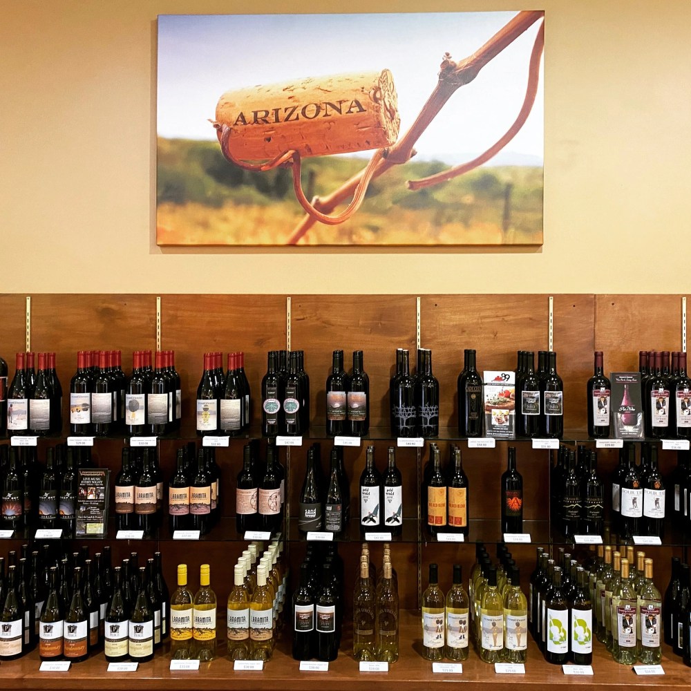 Wine bottles displayed on wooden shelves with a framed cork photo labeled 'Arizona' above.