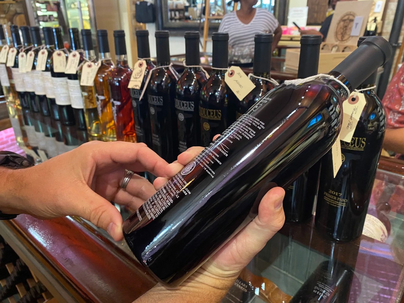 Person holding a wine bottle in a store with more bottles lined up on the counter.